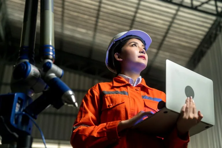 Engenheira com capacete utilizando notebook em industria 4.0